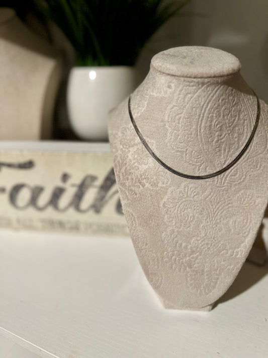 Necklace displayed on a textured stone bust with a blurred 'Faith' sign in the background.